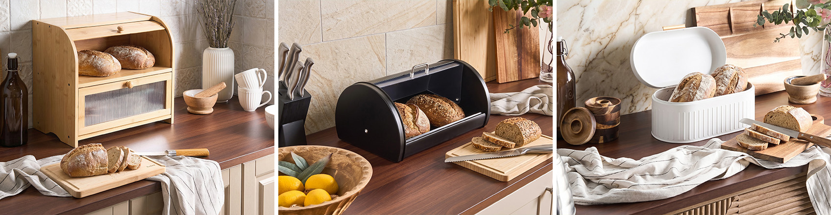 Three bread bins displayed on wooden kitchen countertops: a natural bamboo bread box with fluted front panel, a black metal roll-top bread box, and a white bread box with ribbed detail