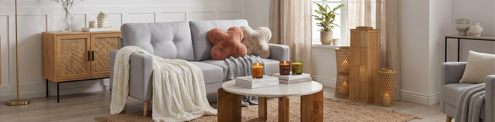 An image showing a calm living area with a sofa adorned by blankets and decorative cushions and a coffee table in front of it