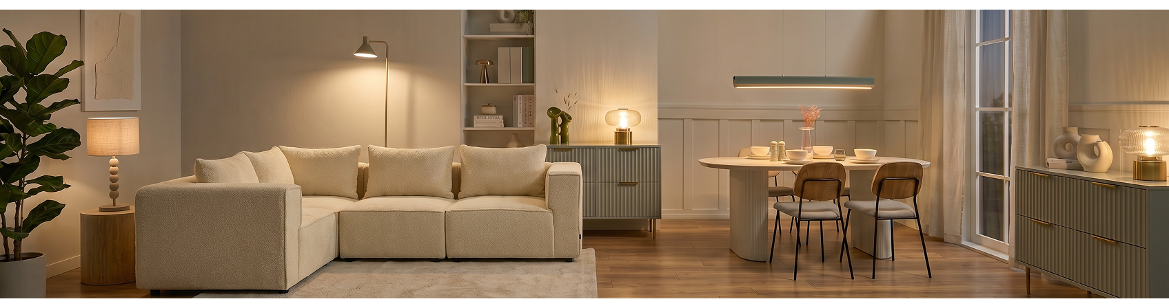 Living and dining room with a cream sectional sofa, a white dining table, and fluted green consoles under warm lighting.